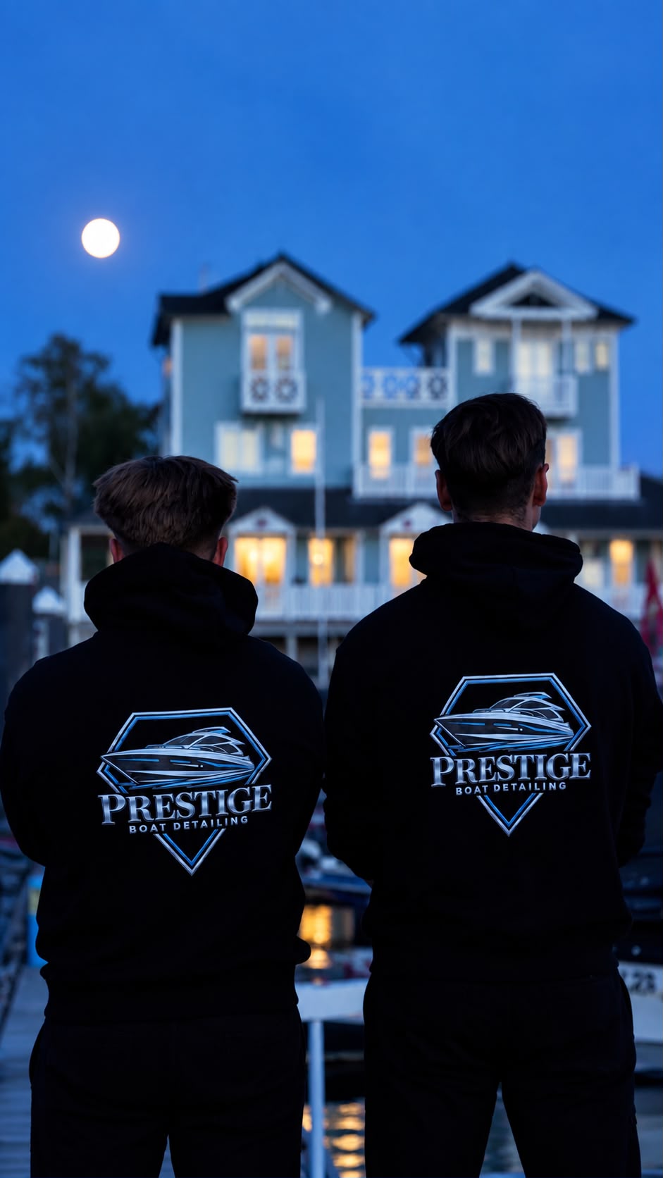 Oli und Aleks von hinten in Prestige-Hoodies mit Logo, vor dem Hafenhaus bei Mondschein